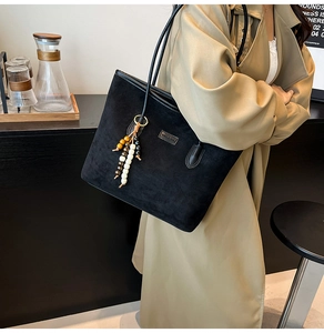 Detail of black suede tote bag with beaded tassel charm and metal logo on a model