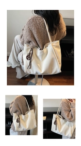 Detail of white leather tote bag featuring elegant decorative ribbon and charm attachment