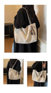 Detail of beige large capacity tote bag with logo pendant worn by a model