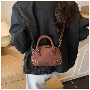 Sac bowling mini en daim marron avec clous porté en bandoulière par un modèle