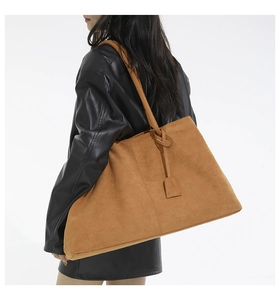 Détail d'un grand sac fourre-tout en daim marron porté à l'épaule sur une veste en cuir