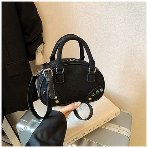 Détail du sac bowling en daim noir avec clous colorés sur une valise argentée