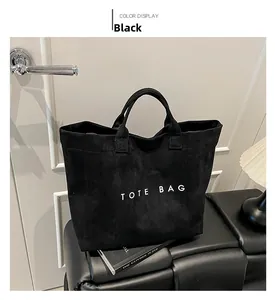 Detail of a large black suede tote bag with white TOTE BAG lettering and sturdy handles