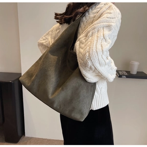 Detail view of large dark olive suede tote bag carried by a model in a minimal setting