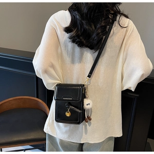 Close-up of black crossbody bag with knot decor and white plush charm on model