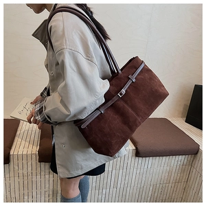 Détail d'un grand sac cabas en daim marron avec bandoulière porté à l'épaule