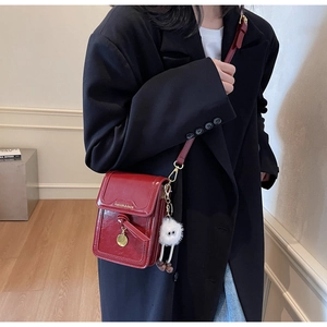 Detail of red glossy shoulder bag with gold lettering and white pompom on black suit