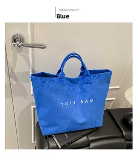 Detail of blue suede tote bag with white text placed on a black leather bench