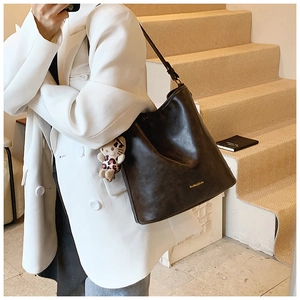Detailed view of black leather shoulder bag with gold logo and leopard plush charm
