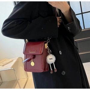 Detail of burgundy glossy leather bag with gold metal trim and plush charm