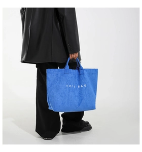 Detail of blue suede tote bag with white text print held by a model in a leather coat