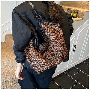 Detail of leopard print tote bag featuring black leather straps and heart charm