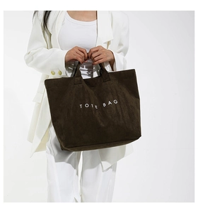 Detail of large dark brown corduroy tote bag held by model in white suit