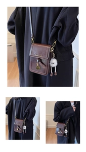 Detail view of brown crossbody bag with gold charms and a cute white plush monster pendant