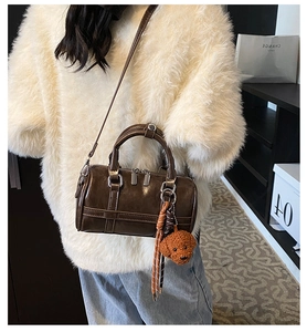 Brown Boston handbag detail showing glossy leather, plush bear charm, and shoulder strap