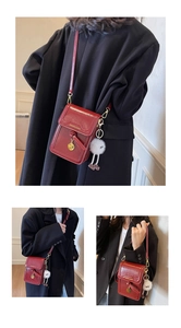 Detail of red glossy leather phone bag with gold tassel and white plush charm accessory