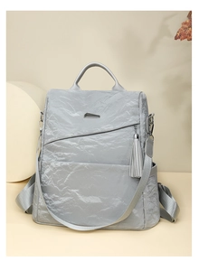 Detail of silver metallic fashion backpack featuring tassel ornament and metal hardware