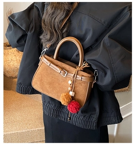 Close-up of brown suede crossbody bag with decorative plush pom-poms and metal hardware
