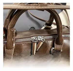 Macro view of silver double zippers and smooth PU leather handles on a dark brown bag