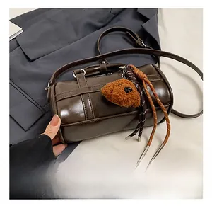 Detail of dark brown bowling bag with plush bear charm and woven cord on white surface