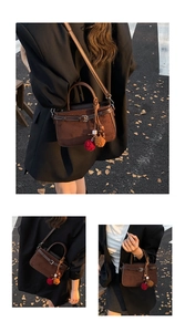 Close-up of dark brown suede handbag with decorative buckle and fuzzy pompom charm detail