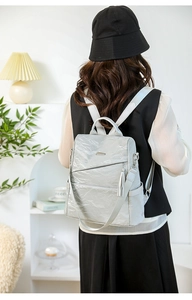 Detail of light gray backpack with wrinkled texture and tassel decoration on person