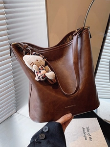 Vintage dark brown leather tote bag with plush cat charm in a minimalist studio setting