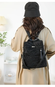 Detailed back view of a black pleated leather backpack worn over a khaki trench coat