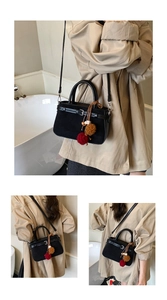 Detail of black crossbody bag with decorative fur pompom charm and top handle strap