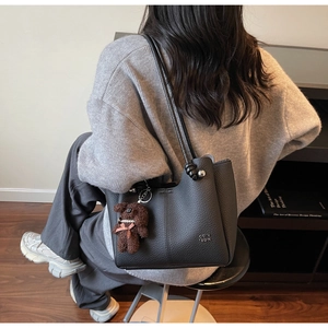 Détail du sac seau en cuir grainé noir avec charme d'ours en peluche et boules argentées