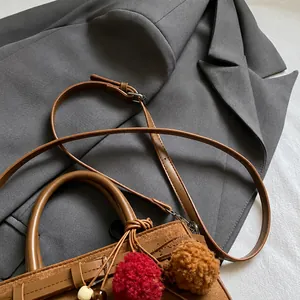 Detail of adjustable shoulder strap and plush charm on brown suede crossbody bag