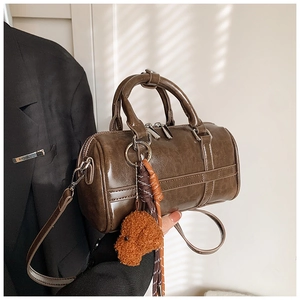 Detail of a brown Boston bag in oil wax leather with teddy bear charm and silver hardware