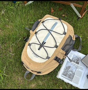 Detail of khaki outdoor backpack with functional elastic cords and side mesh pockets on grass