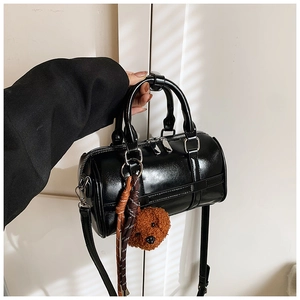 Detail of a black Boston barrel bag with a glossy finish and brown plush bear charm