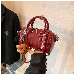 Detail of burgundy Boston handbag with silver zippers and a cute brown bear charm