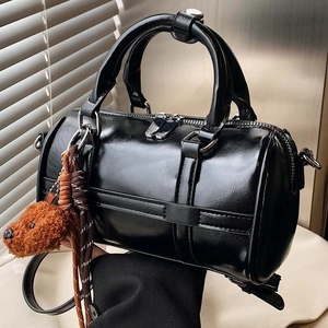 Glossy black Boston handbag with plush bear charm and silver hardware on a modern background