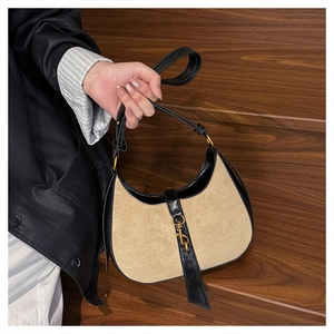 Detail of a beige suede and black patent leather crescent bag with golden clasp hardware