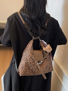 Large leopard print shoulder bag with brown leather flap and bear charm on a female model
