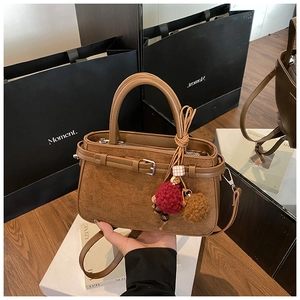 Brown leather handbag with suede panels and pom-pom charm shown in a studio setting
