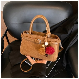 Close-up of brown suede handbag with decorative buckle and plush pompom keychain