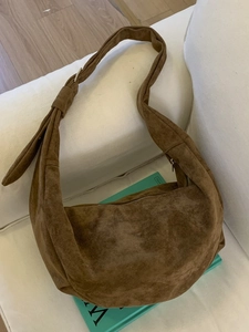 Brown faux suede hobo bag with moon shape and wide shoulder strap on white fabric