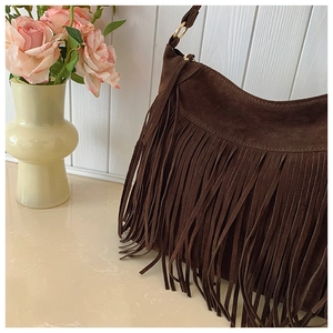 Détail d'un sac à franges en daim marron foncé avec anneaux dorés dans un décor élégant