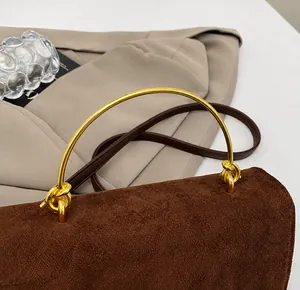 Detail van bruine suède crossbodytas met een gouden halfronde metalen handgreep boven