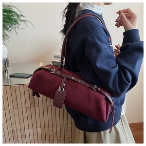 Detail of burgundy suede cylindrical shoulder bag featuring metal buckle and strap texture