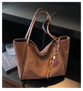 Detail of a brown suede tote bag featuring fringe tassels and a leopard bear charm
