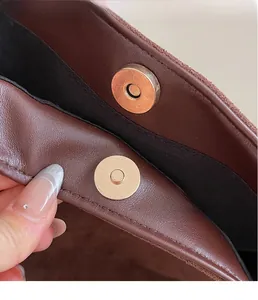 Detailed macro view of the gold-tone magnetic snap closure on a brown leather tote bag