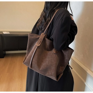 Detail view of large dark brown retro tote bag in matte leather worn by a model