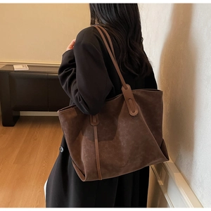 Detail of a large dark brown matte leather tote bag worn by a model in a modern interior
