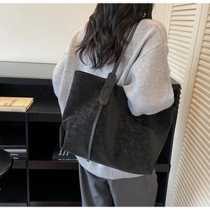 Close-up of minimalist black tote bag with matte leather texture shown on model