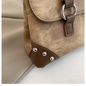Macro detail of khaki twill fabric with brown leather trim and silver rivets on a handbag